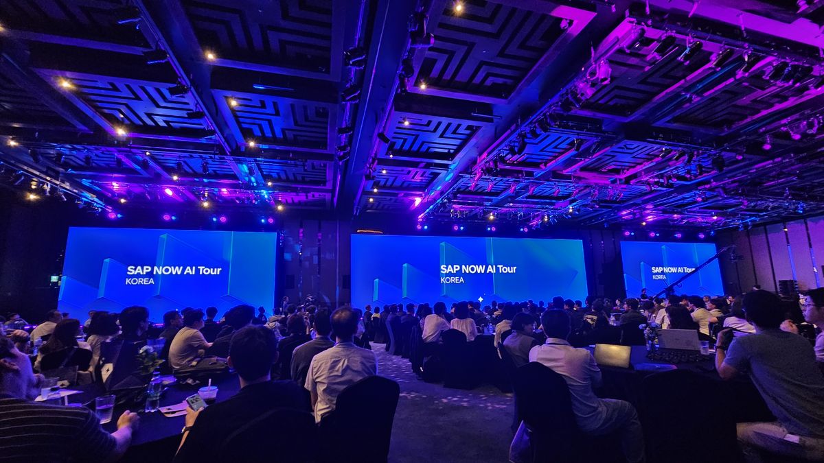 SAP NOW AI Tour Korea 2026 행사장 전경. 대형 스크린 세 개에 'SAP NOW AI Tour KOREA' 로고가 떠 있고 원형 테이블마다 참석자들이 앉아 있다